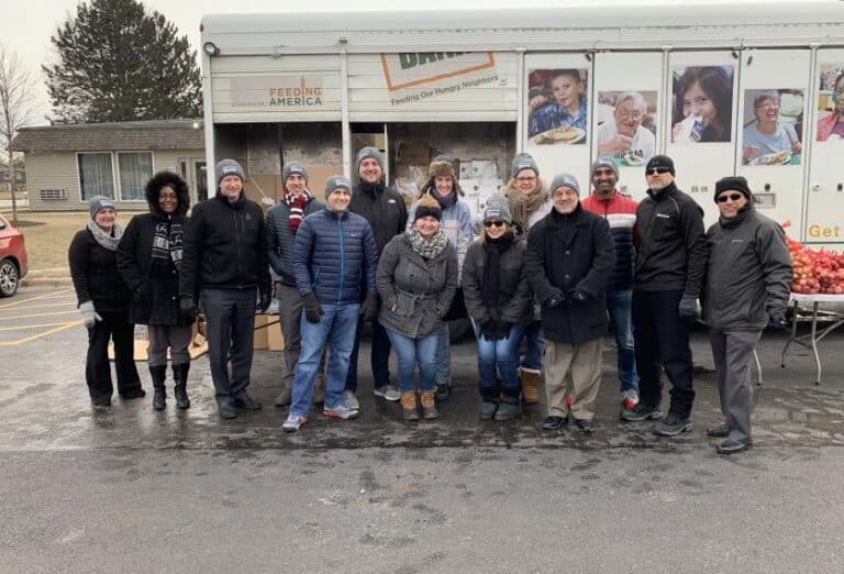 A cheerful group poses in front of a food truck during a Feeding America event