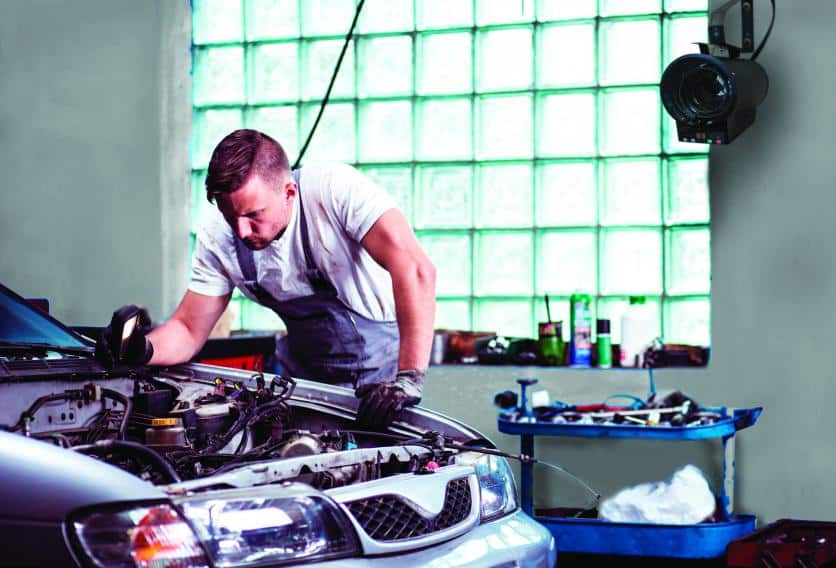 A man is focused on fixing a car in a spacious garage, with various tools and parts visible around him