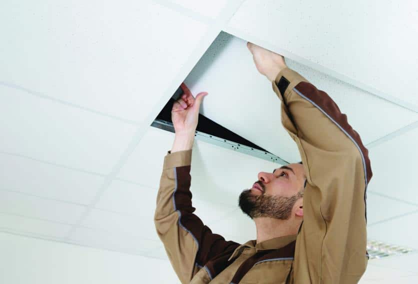 A man is repairing a ceiling tile in a well-lit room