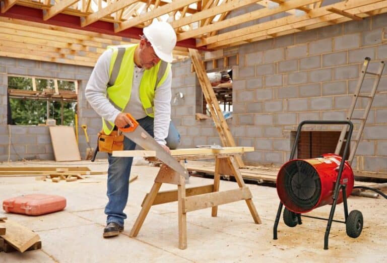 A man wearing a hard hat and safety vest is focused on his work at a busy construction site