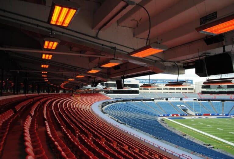 A stadium featuring red seats and a large screen, equipped with infrared heating