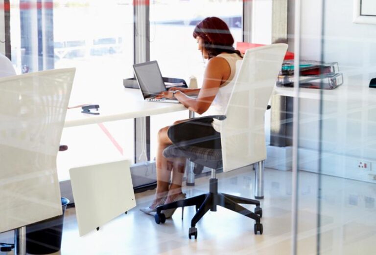 A woman seated at a desk, focused on her laptop, surrounded by a tidy workspace and natural light