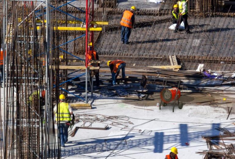 Construction workers in hard hats and safety gear working on a busy construction site with machinery and materials around them