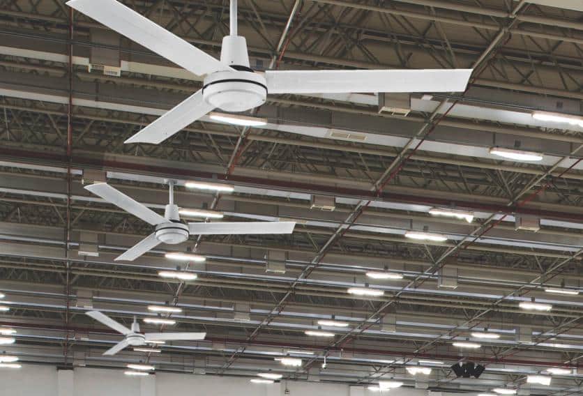 Three large ceiling fans spinning in an industrial warehouse, providing airflow in a spacious, open environment.