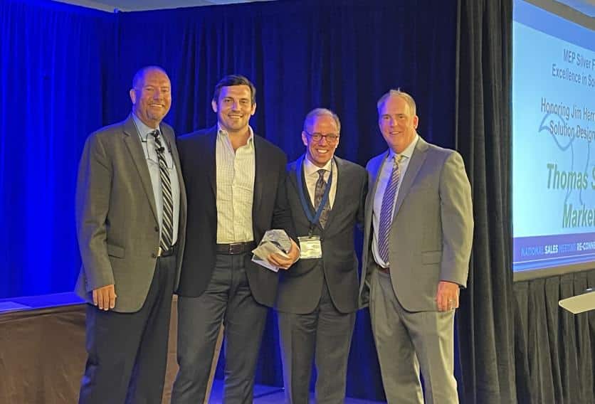 four men positioned on stage during a business event posing for photo